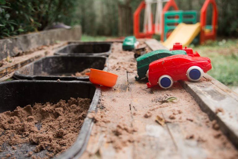 Colorful toy cars scattered in an outdoor sandbox, creating a playful scene.