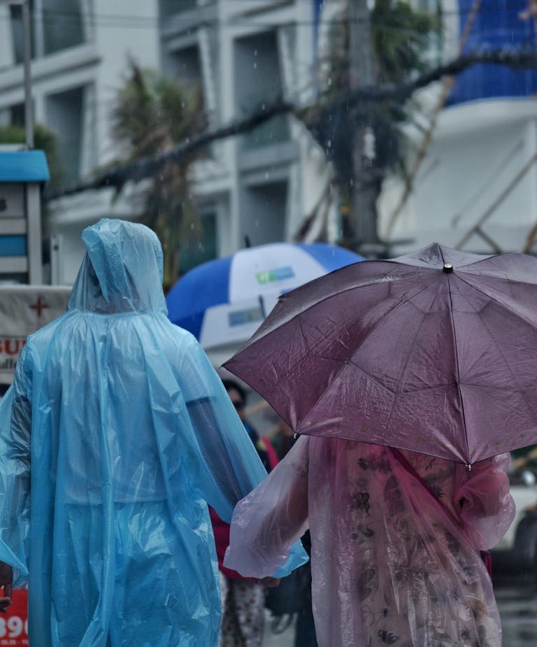 People wearing colorful ponchos and umbrellas in heavy rain, city background.