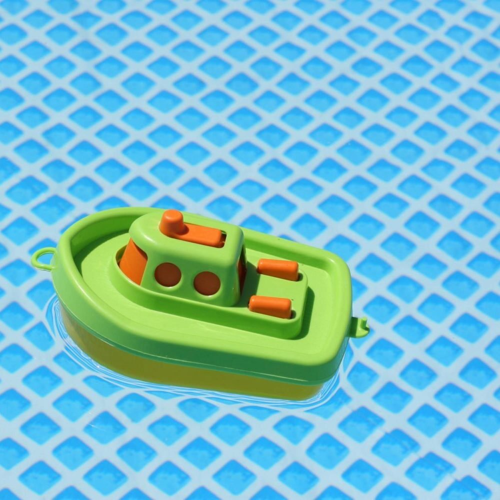 Vibrant plastic toy boat floating in a grid-patterned blue swimming pool.