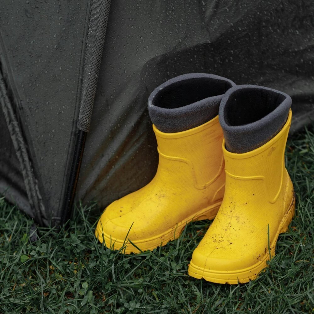 Vibrant yellow rain boots beside a wet tent on green grass, perfect weather gear imagery.